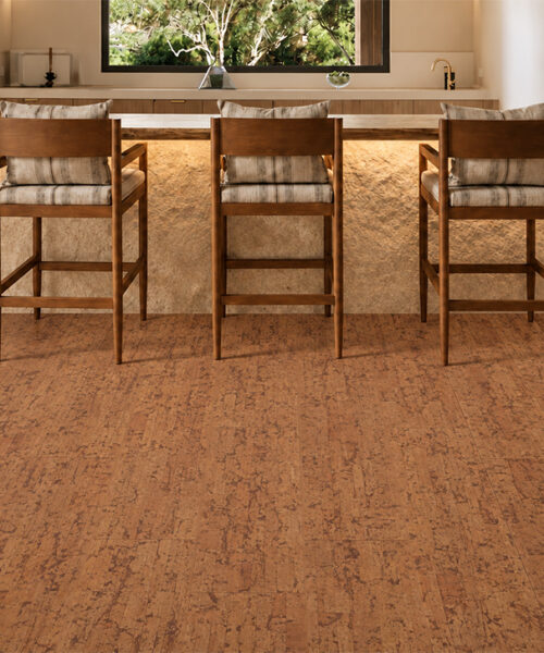 Medium-Brown Amber Streak Floating Cork Flooring Surrounds An Illuminated Stone Home Bar With Three Cushioned Wooden Stools.