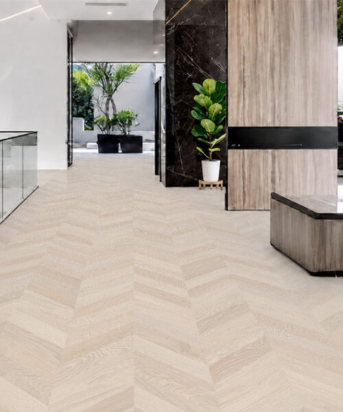 Clara Chevron Swiss Design Cork Floating Flooring Brightens A Modern Hallway With Glass Railings And Indoor Plants.