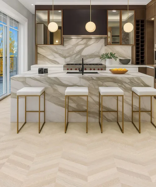 Modern Kitchen With Marble Island And Clara Chevron Cork Floating Flooring In A Light Natural Tone.