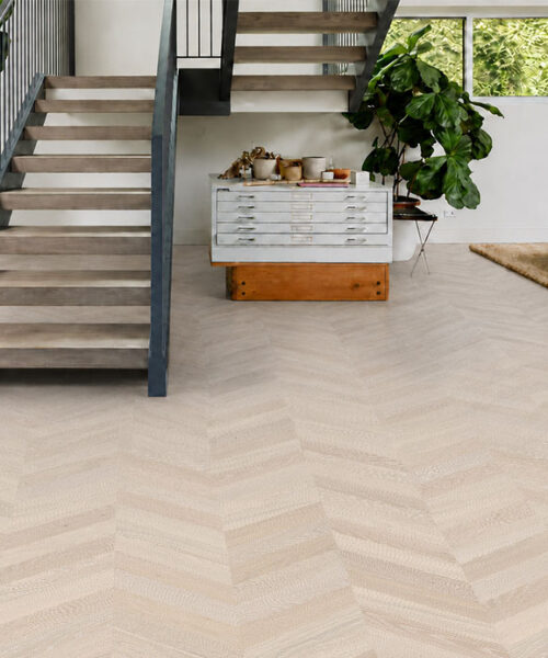 Light gray Clara Chevron cork flooring surrounds an open staircase, gray sofa, and large leafy plants.