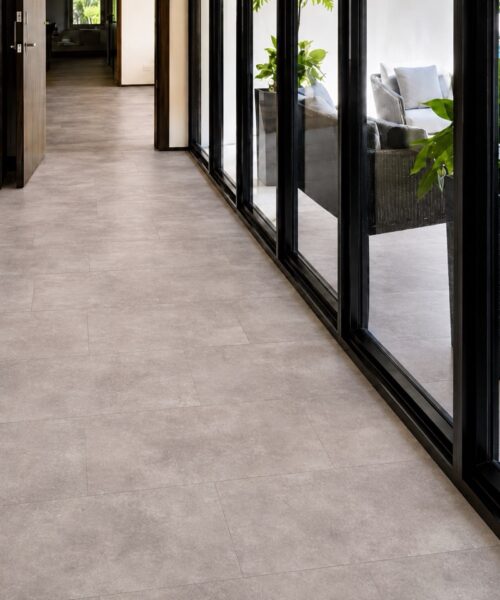 Copperstone Gray Natural Composite Flooring With Subtle Stone-Look Variation Extends Through A Glass-Lined Hallway Beside A Pool Patio.