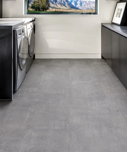 Gray concrete look floating flooring between contemporary laundry cabinets and appliances