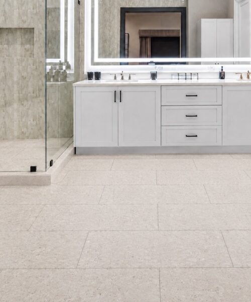 Matera Blend mineral-based flooring in light limestone features subtle printed variation beneath a white bathroom vanity and glass shower.
