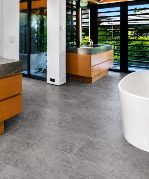 Midnight Slate Swiss Techslate Flooring Pairs A Gray Slate-Look Pattern With A Freestanding Bathtub, Wood Vanities, And Tropical Glass Views.