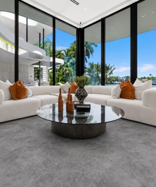 Midnight Slate Stone-Look Flooring With Subtle Gray Mineral Variation Surrounds Curved White Sofas In A Bright Contemporary Living Room With Glass Walls