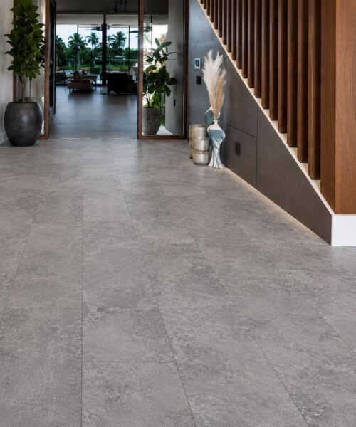 Midnight Slate Click-Lock Flooring Runs Through A Modern Foyer With Gray Stone-Look Planks, Wood Stairs, Planters, And A Glass Entry Door.