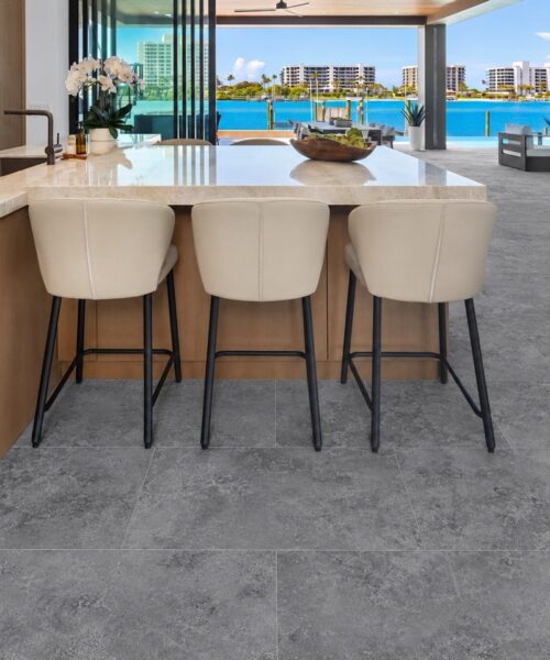 Midnight Slate Waterproof Floating Flooring Extends Through A Modern Kitchen With An Island, Bar Stools, And Expansive Waterfront Windows.