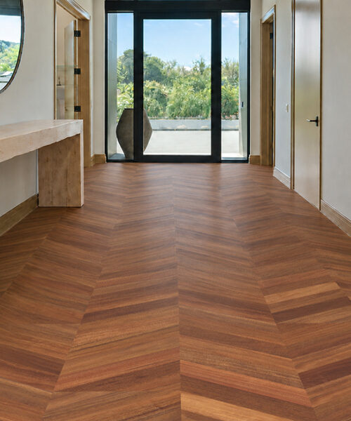 Noble Chevron Swiss Design Cork Floating Flooring Displays Rich Walnut Chevrons In A Hallway With A Wood Console.