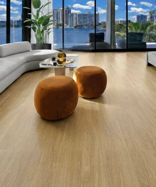 Sandstorm Swiss Design cork floating flooring in a luxury waterfront bedroom featuring light oak wood grain, a curved white sofa, floor-to-ceiling windows, and a modern platform bed.