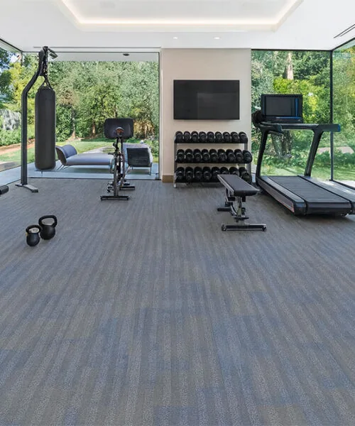 Home gym with Serpent Luxe Forna Swiss leather flooring, durable floating planks in blue-gray tones, complementing fitness equipment and large glass windows.