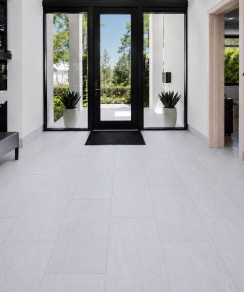 Snowstone - 19/64&Quot; (7.5Mm) - Swiss Techslate (Mcsnows7.5) Snowstone Click-Lock Flooring Features Pale Gray Mineral Texture In A Modern Entryway With Black-Framed Doors, A Bench, And Console Table.