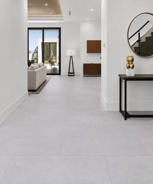 Snowstone contemporary architectural flooring forms a staggered pale gray plank layout through a hallway beside a staircase and console table.