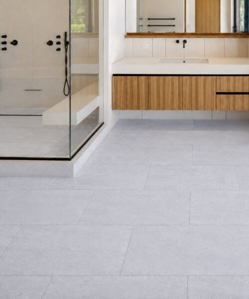 Snowstone - 19/64&Quot; (7.5Mm) - Swiss Techslate (Mcsnows7.5) Snowstone Waterproof Floating Flooring Shows A Pale Gray Concrete-Look Pattern In A Modern Bathroom With A Glass Shower And Wood Vanity.