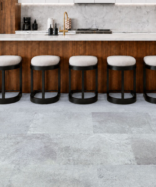 Warm Stone light gray stone-look cork planks extend across a walnut kitchen with a marble island and stools.