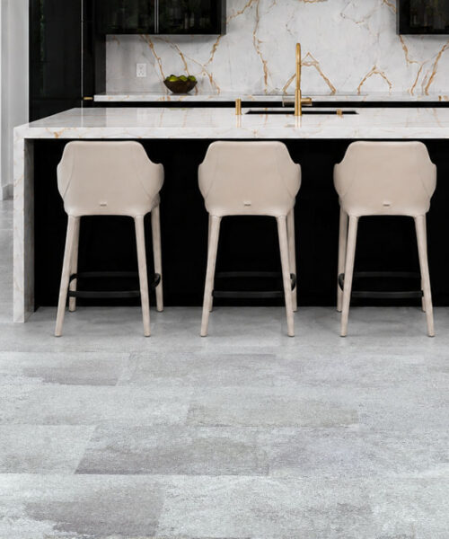 Warm Stone - 7/16&Quot; (11Mm) - Swiss Design Cork Floating (Fwmst11) Warm Stone Light Gray Stone-Look Cork Flooring Complements A Black Kitchen With Marble Island And Cream Stools.